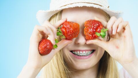 Alle Augen auf die Erdbeeren? Mädchen häl sich Erdbeeren vor die Augen und lächelt breit dabei