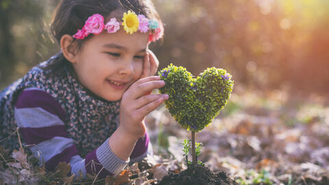 Mädchen liegt im Garten und untersucht Buchsbäumchen in Herzform