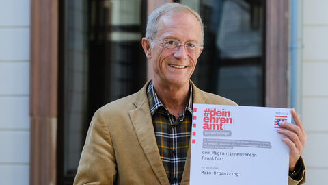 Staatsminister Axel Wintermeyer hält den Förderbescheid in den Händen und lächelt in die Kamera.
