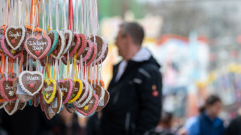 Viele Lebkuchenherzen hängen an einer Bude herunter, im Hintergrund Besucher