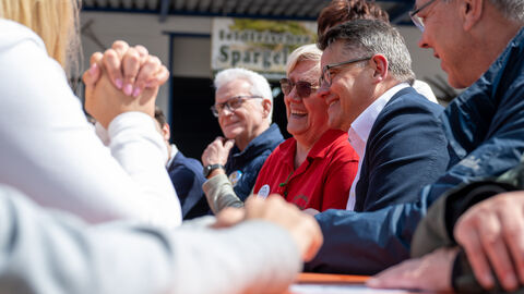 Ministerpräsident Rhein sitzt lächelnd am Tisch neben Teilnehmern der Spargelwanderung