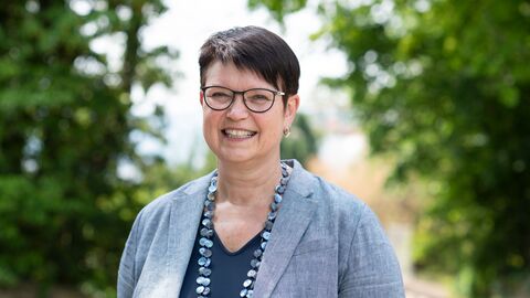 Portrait von Regine Bresler, sie steht im Freien vor Bäumen und lächelt.