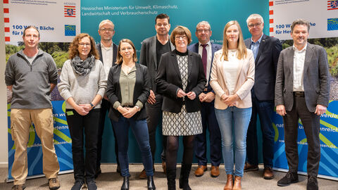 Mehrere Personen stehen zum Gruppenfoto aufgestellt vor einer türkisen Pressewand. Darunter Ministerin Hinz und Personen des Ministeriums sowie der HLG.