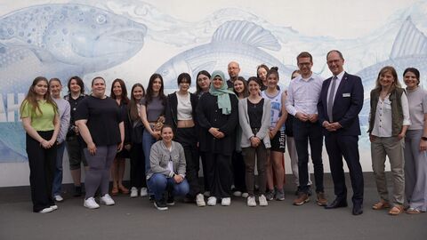 Schülerinnen, Schüler und Lehrer der Alicenschule Gießen, Staatssekretär Michael Ruhl, Regierungspräsident Dr. Christoph Ullrich und Mitarbeiterinnen RP Gießen Marlene Höfner und Elisabeth Kister stehen vor einer Wand zum Gruppenfoto aufgestellt. Auf der Wand im Hintergrund sind Fische aufgemalt.