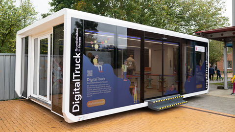 DigitalTruck Ein Container-Anhänger aus Glas mit der Aufschrift "DigitalTruck - Grundschultour in Hessen" steht auf einem Schulgelände.