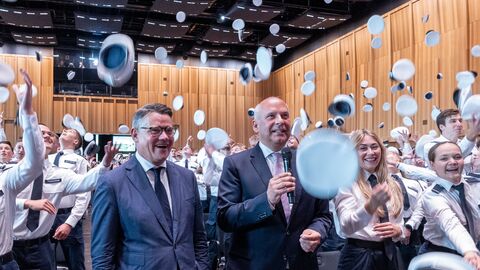 Ministerpräsident Boris Rhein und Innenminister Roman Poseck stehen inmitten von Menschen, die ihre Mützen in die Luft werfen. 