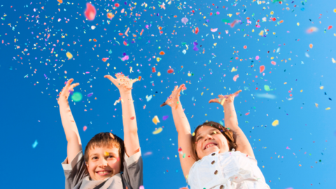 Hurra, wir feiern Zwei fröhliche Kinder werfen buntes Konfetti in die Luft.