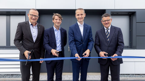 Ministerpräsident Boris Rhein bei der Eröffnung des neuen Reinraums der Firma Zeiss SMT in Roßdorf. Vier Männer stehen in Anzügen gekleidet nebeneinander. Vor ihnen ist ein blaues Band gespannt, das sie mit einer Schere durchschneiden wollen.