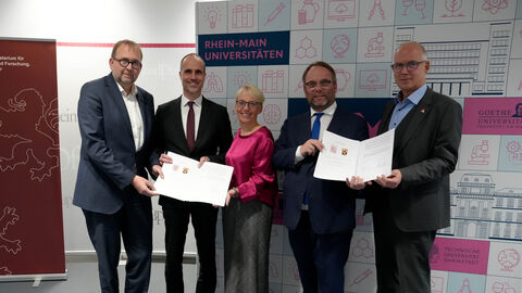 v.l.n.r.: Prof. Dr. Enrico Schleiff (Präsident der Goethe-Universität Frankfurt und amtierender RMU-Sprecher), Clemens Hoch (Rheinland-Pfälzischer Minister für Wissenschaft und Gesundheit), Prof. Dr. Tanja Brühl (Präsidentin der TU Darmstadt), Timon Gremmels (Hessischer Minister für Wissenschaft und Forschung, Kunst und Kultur) und Prof. Dr. Georg Krausch (Präsident der Johannes Gutenberg-Universität Mainz).  Fünf Personen stehen nebeneinander und halten zwei Urkunden hoch.