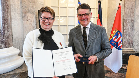 Eine Frau und ein Mann stehen nebeneinander und halten eine Urkunde hoch.