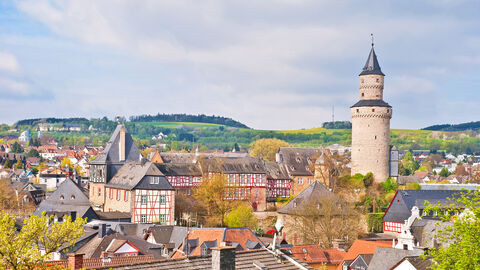 Blick auf ein Dorf. Im Hintergrund sind Wiesen zu sehen und ein großer Turm ragt zwischen den Häusern hervor.