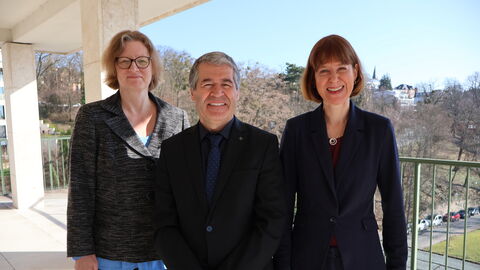 Drei Personen stehen auf einem Balkon nebeneinander.