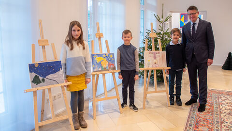 Ministerpräsident Boris Rhein mit drei kindern, die neben Leinwänden und ihrer selbstgemalten Kunst stehen.