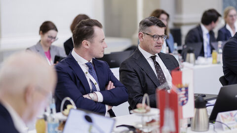 Ministerpräsidentenkonferenz Berlin 2025 Zwei Männer sitzen in Anzügen nebeneinander. Der rechte schaut nach vorne, während der linke den anderen ansieht.